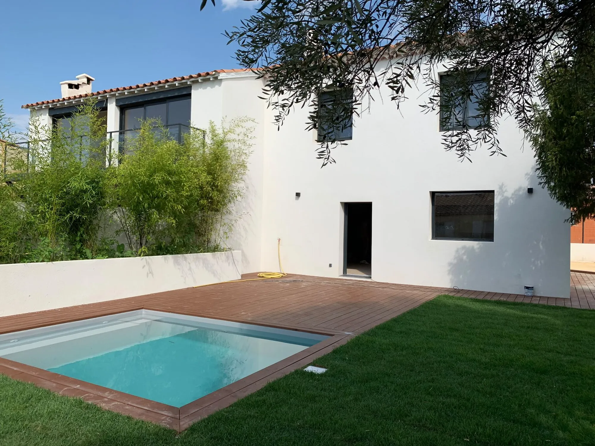 Maison rénovée en blanc avec piscine, terrasse bois et pelouse